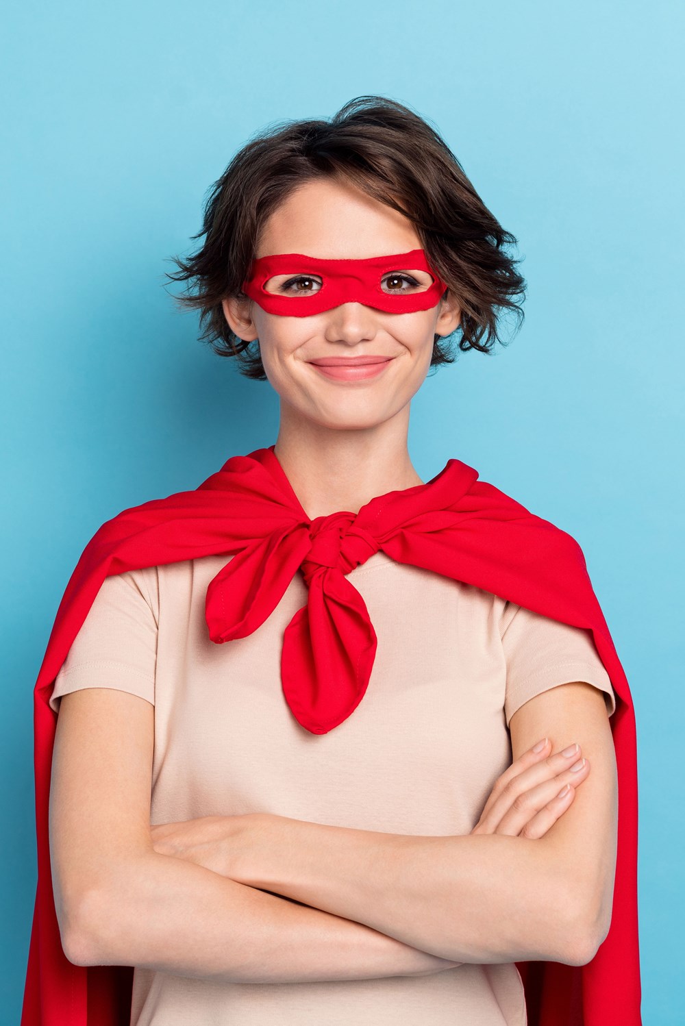 alt="Jonge vrouw in superheld outfit gekruiste armen glimlach"