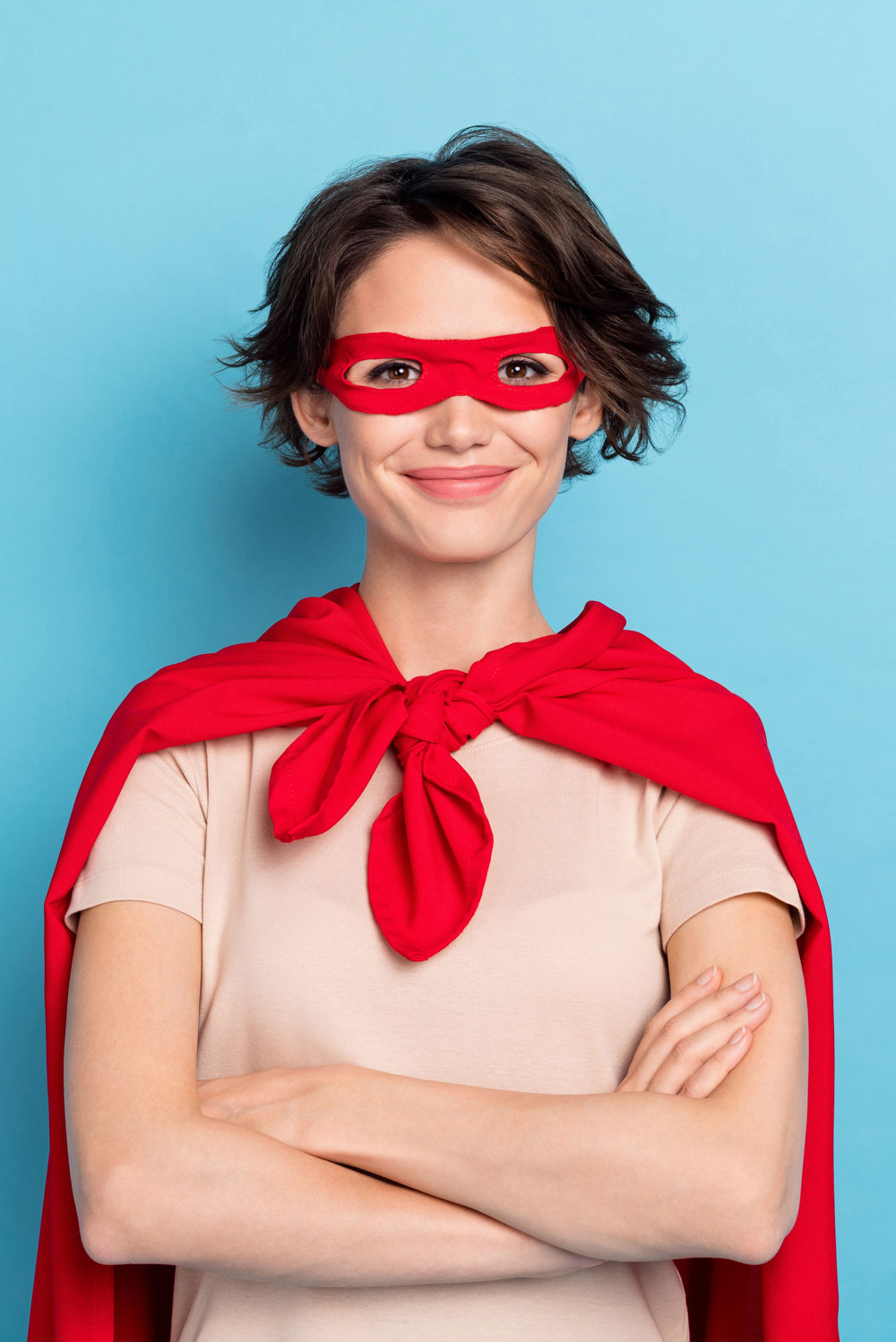 alt="Jonge vrouw in superheld outfit gekruiste armen glimlach"