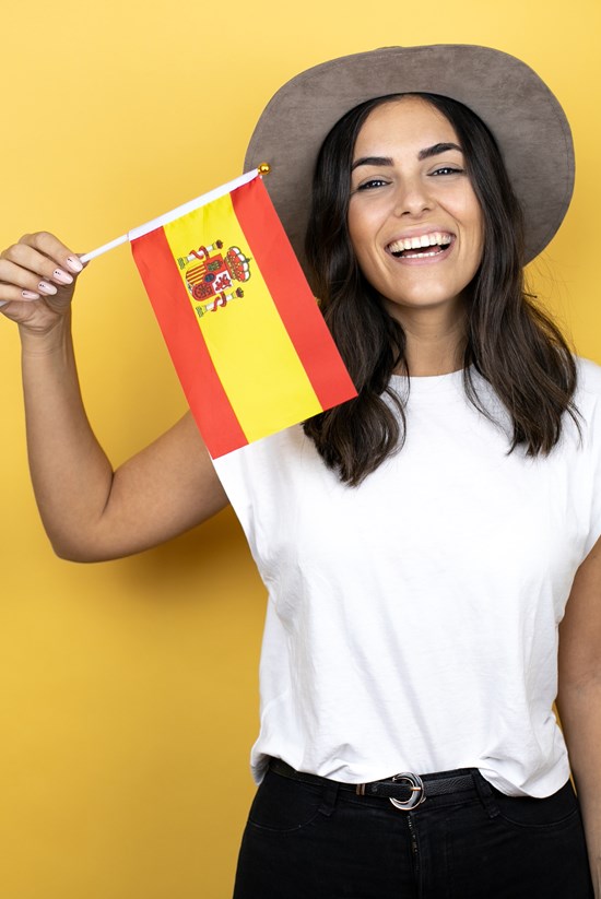 alt="glimlachende vrouw met zonnehoed op en Spaanse vlag in de hand"