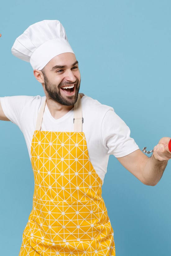 alt="jonge man met koksmuts en schort maakt dansend gebaar"