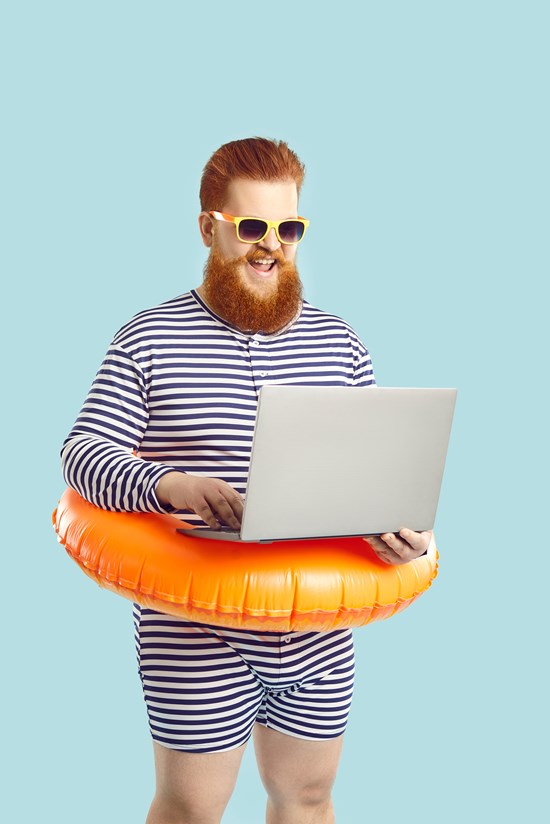 alt="man met rosse baard en zonnebrik draagt gestreept badpak en oranje zwemband met laptop in de handen"