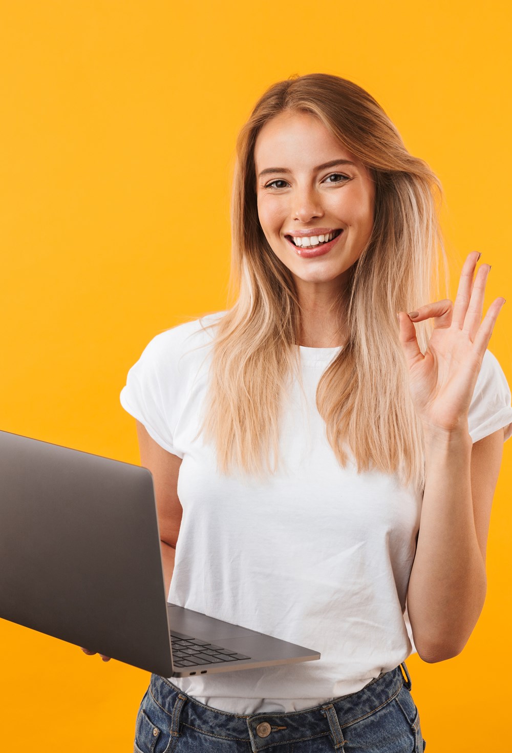 alt="jonge vrouw houdt laptop in de ene hand en steekt andere hand begroetend op"